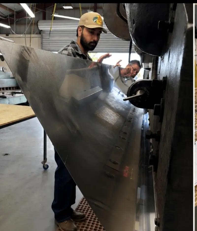 Iron Sight fabricators feeding a stainless steel sheet through the press brake in the Santa Clarita shop